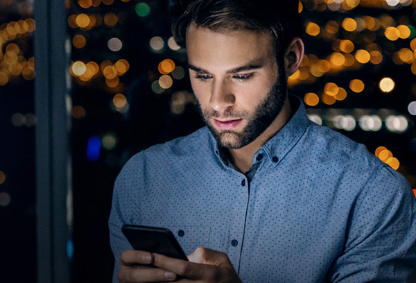 Man in a dark office with face illuminated by smartphone screen